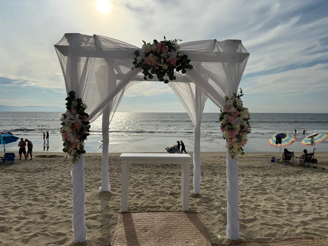 Arco de ceremonia con tela blanca y ramos de flor rosa y blanca frente al mar, Riviera Nayarit