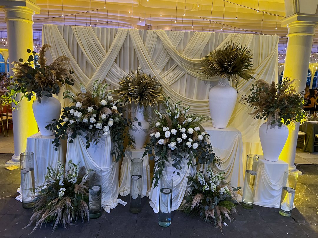 Fondo de tela para la ceremonia: telas marfil cruzadas con jarrones blancos, pampas, rosas y velas, Zapopan
