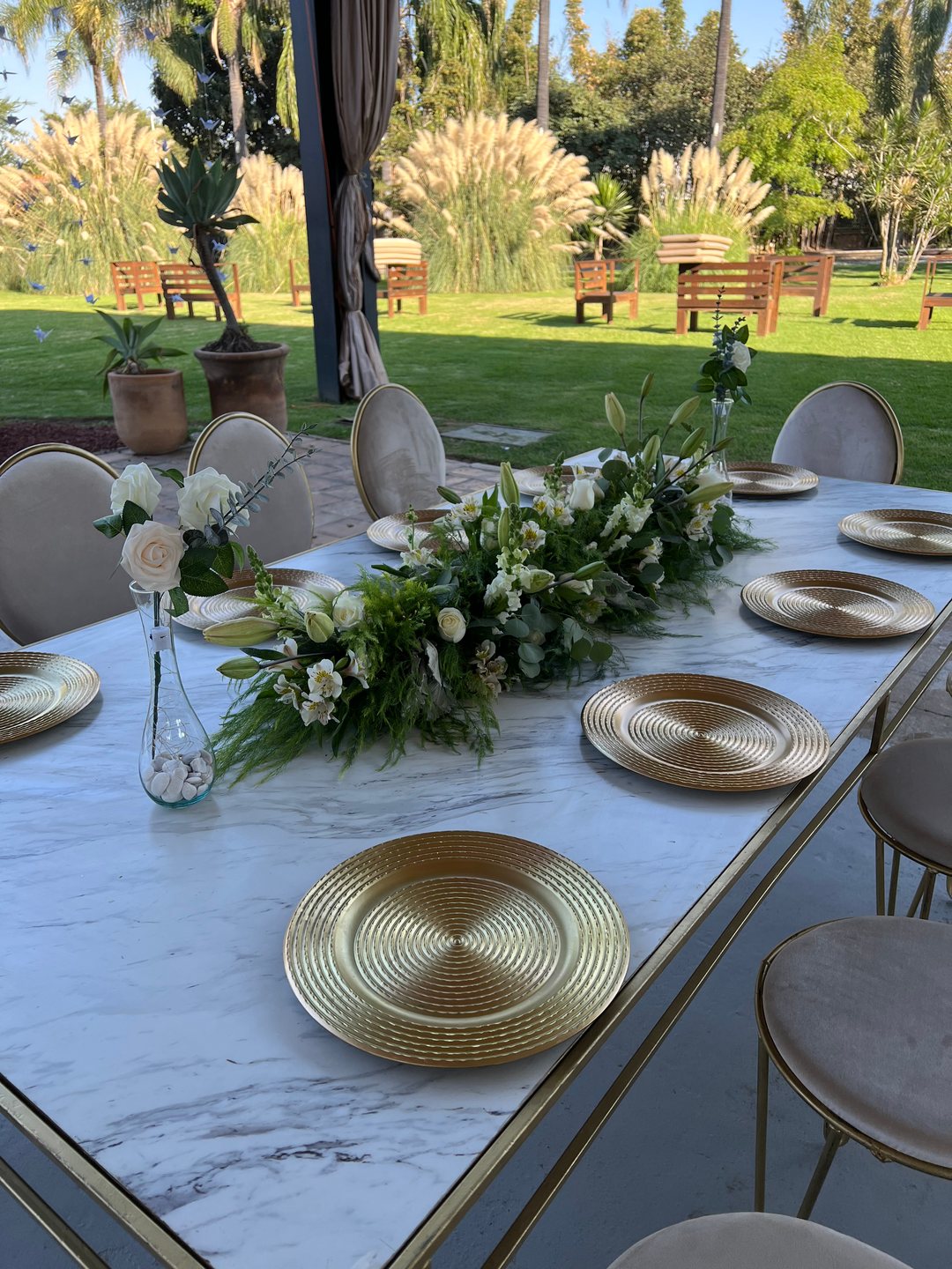 Centro de mesa bajo de flor blanca sobre mesa de mármol con platos dorados, jardín en Zapopan