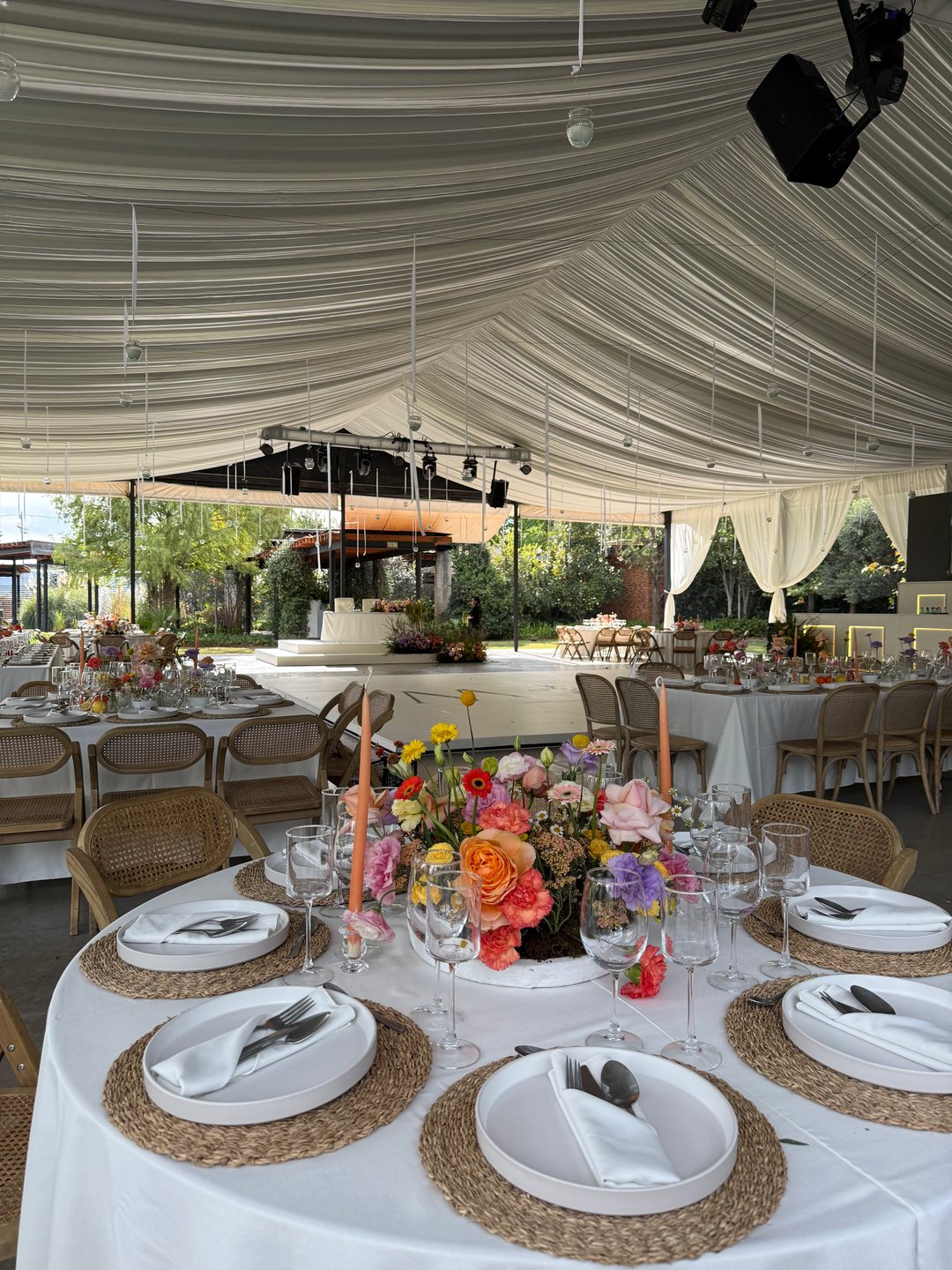 Centro de mesa de flor de colores con velas naranjas bajo un entelado blanco en ondas, terraza en Tlajomulco