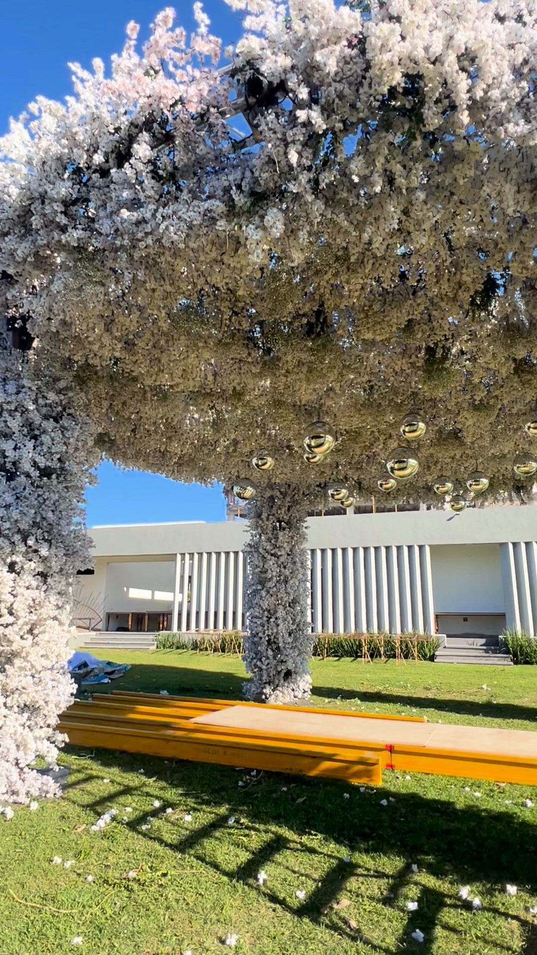 Domo de flor blanca nevada sobre columnas forradas de flor, con esferas de espejo colgando, en un jardín