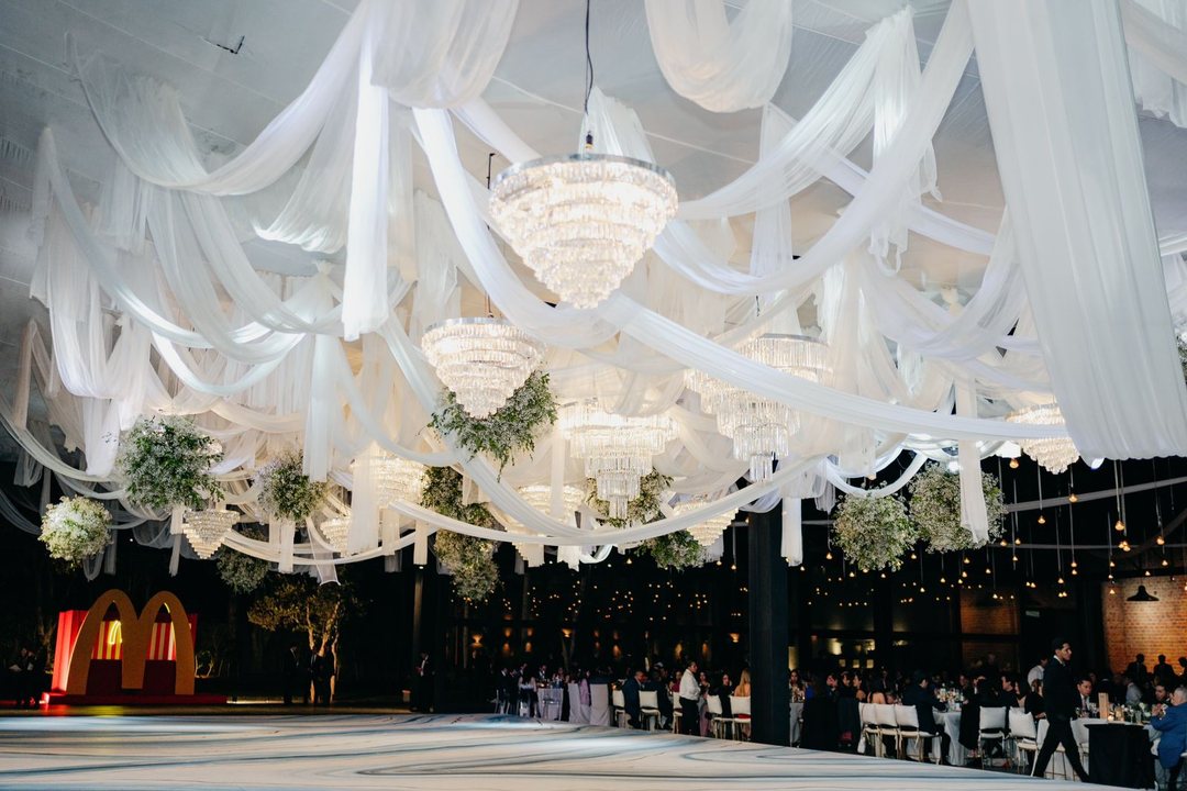 Drapeado de tela blanca con candiles de cristal y follaje sobre el salón de noche