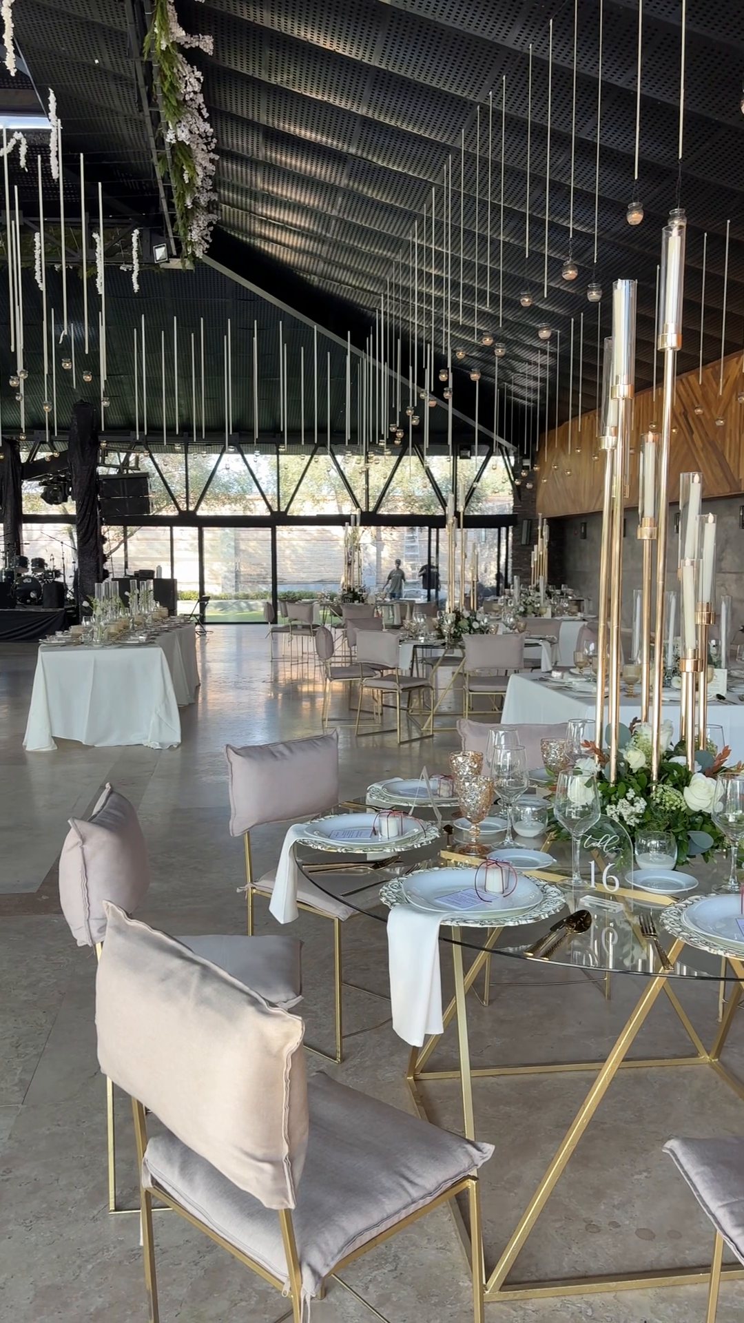 Salón de cristal con cientos de hilos colgantes de flor y follaje sobre mesas con candelabros altos