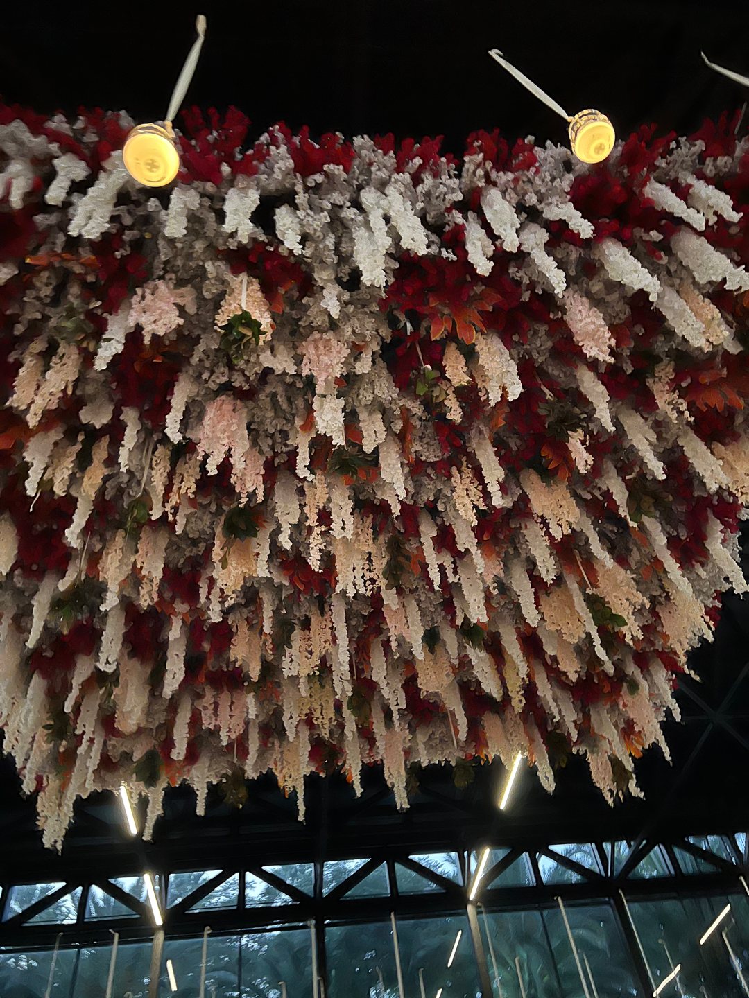 Jardín colgante de flor blanca, crema y roja con veladoras sobre la pista de un pabellón de cristal, de noche
