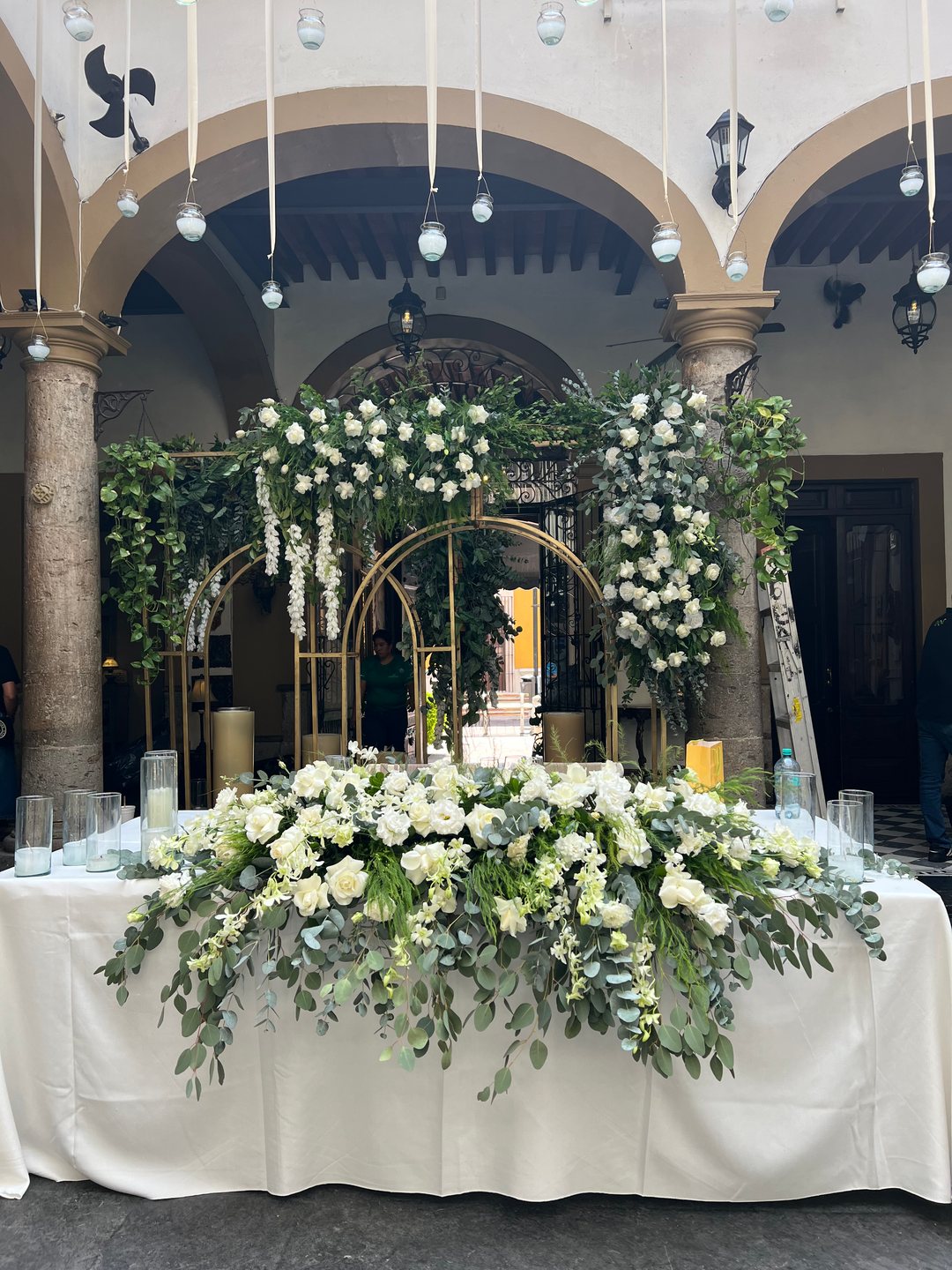 Mesa de honor con arreglo largo de flor blanca y arco dorado de flor y follaje detrás, Guadalajara
