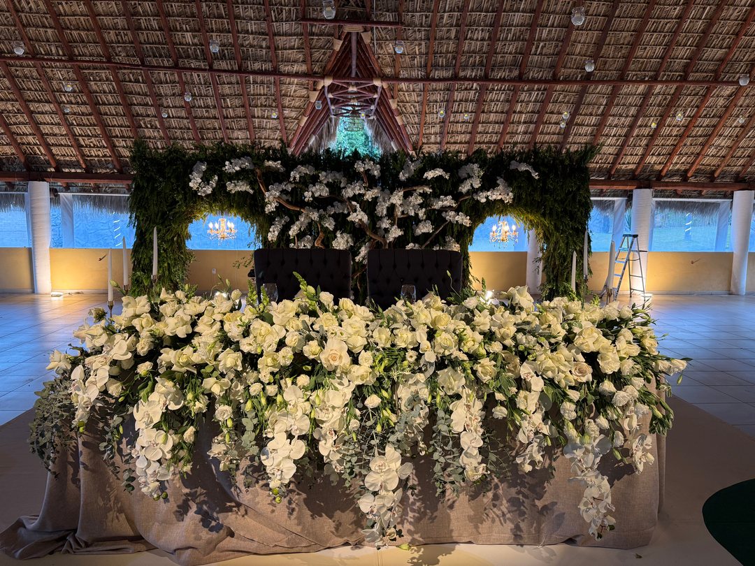 Mesa de honor con orquídeas y rosas blancas, muro de follaje y ramas con orquídea bajo una palapa, Zapopan