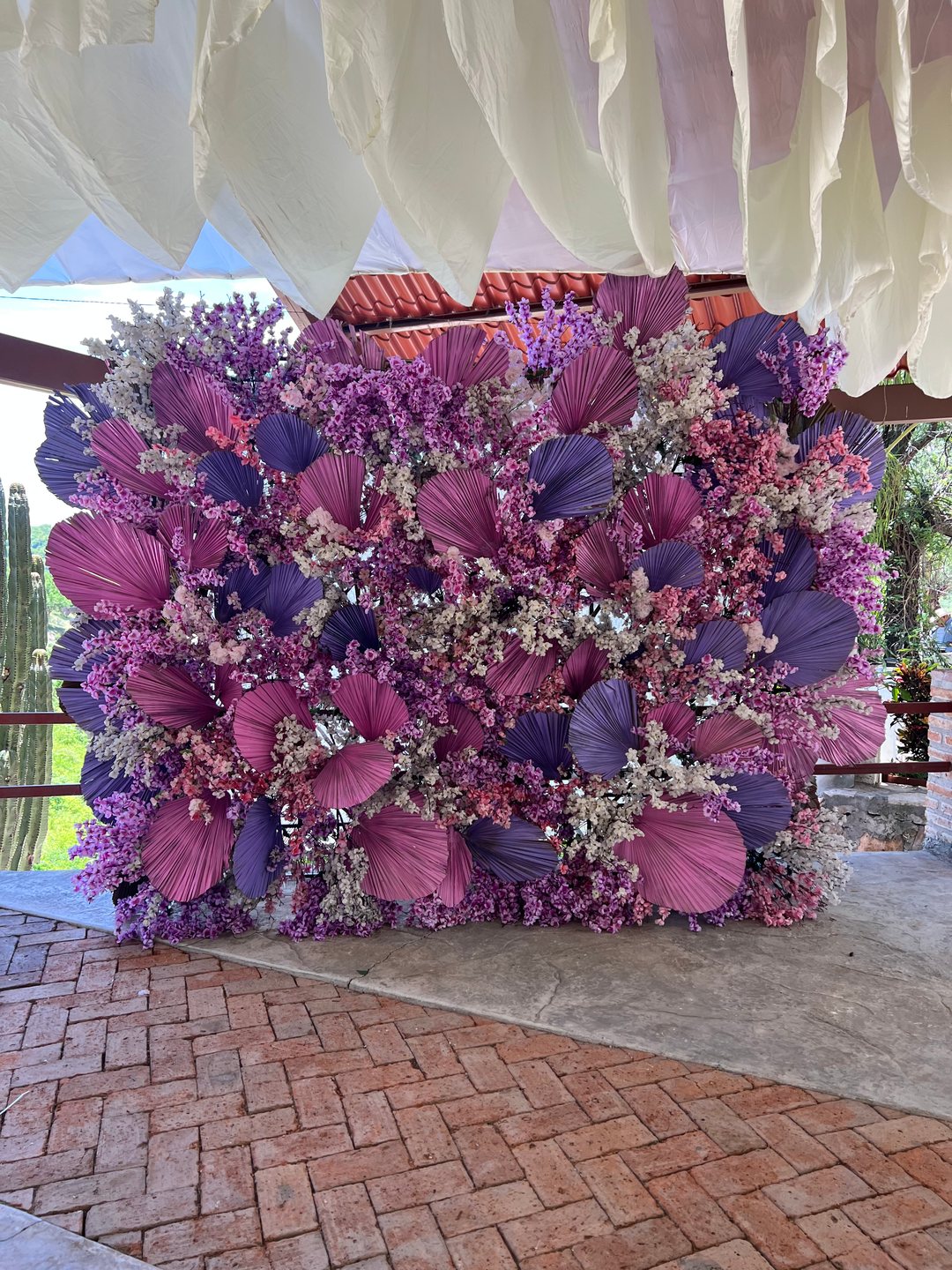 Muro floral morado, rosa y lila con hojas de palma bajo un entelado blanco, terraza en Zacatecas