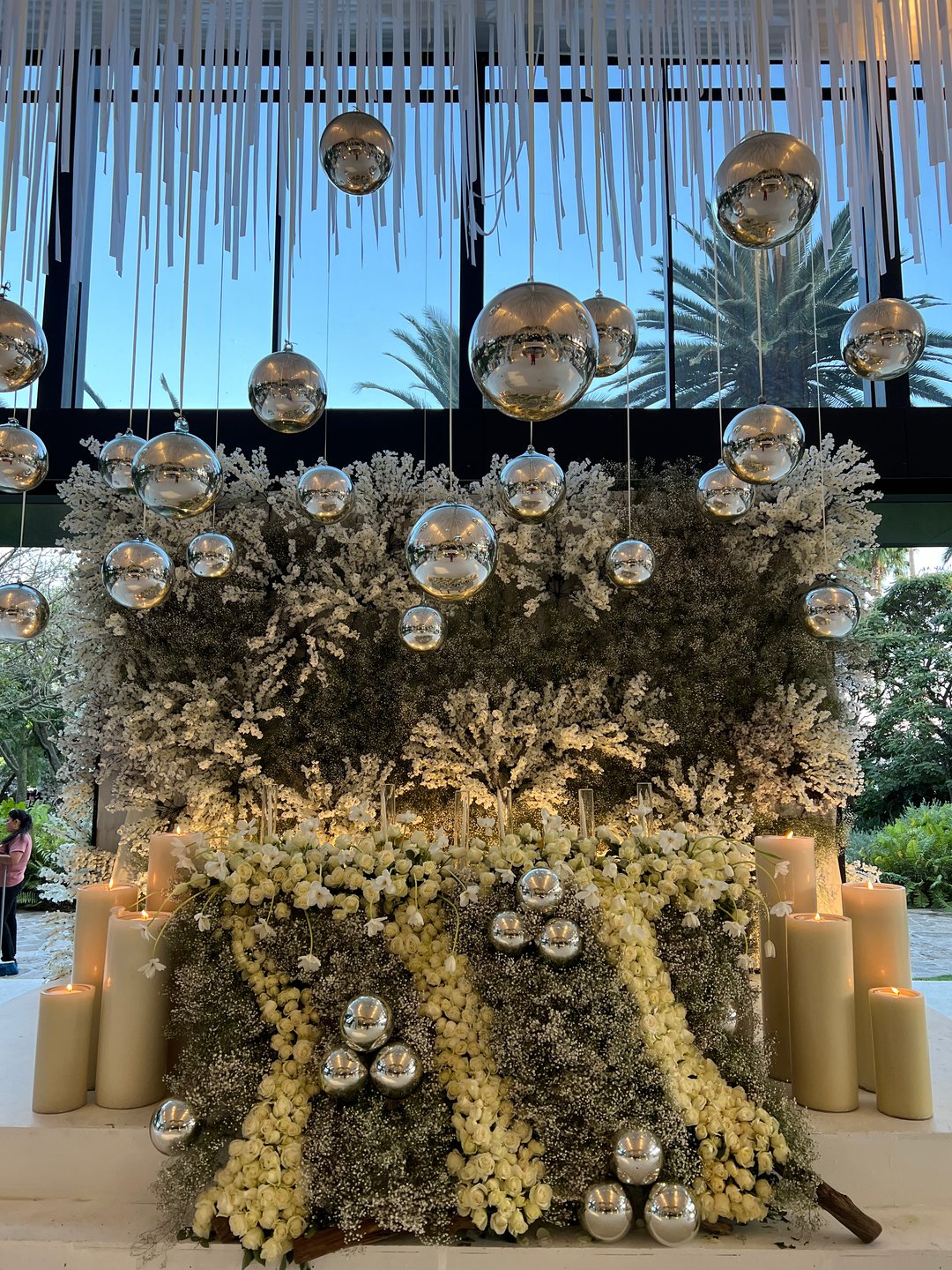 Muro de follaje con flor blanca y amarilla, esferas de espejo y tiras de tela colgantes, Tlajomulco