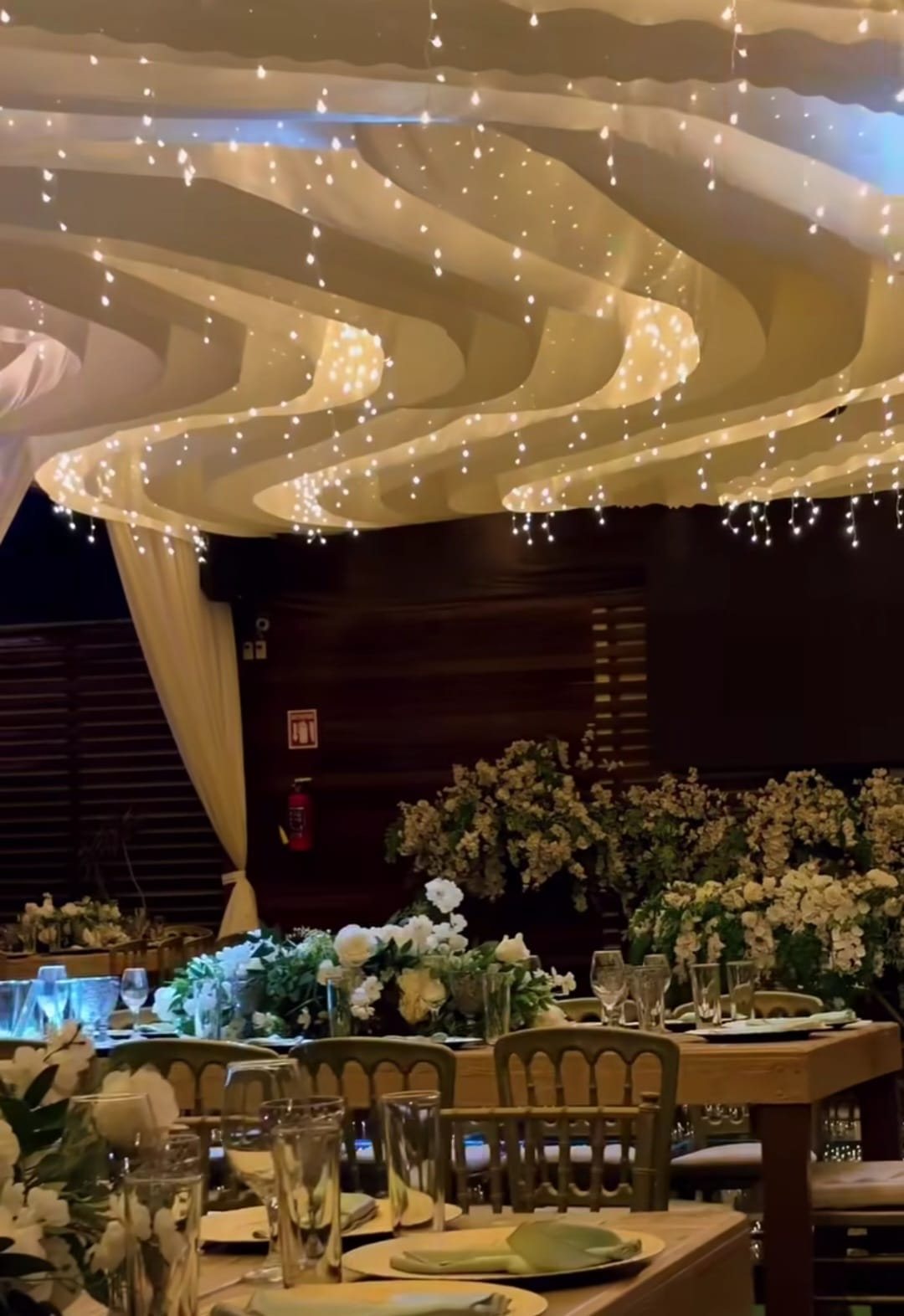 Ondas de tela blanca con series de luz sobre mesas con flor blanca