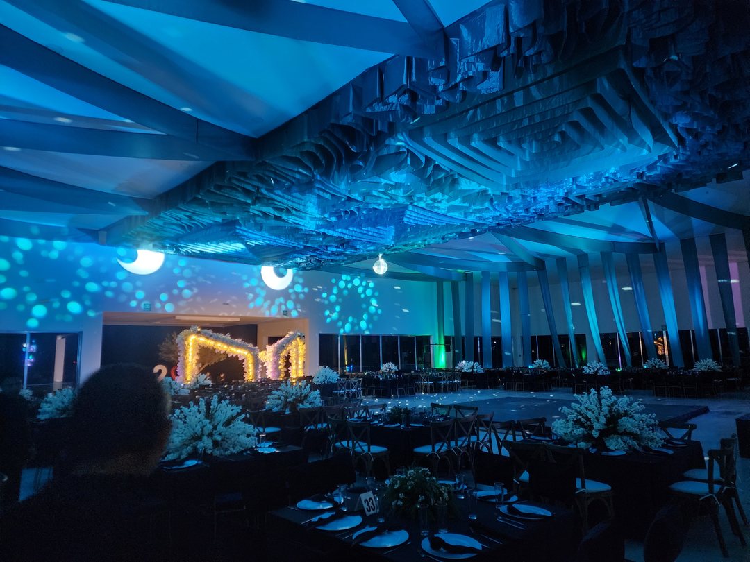 Salón de noche con el techo de tela iluminado de azul sobre las mesas