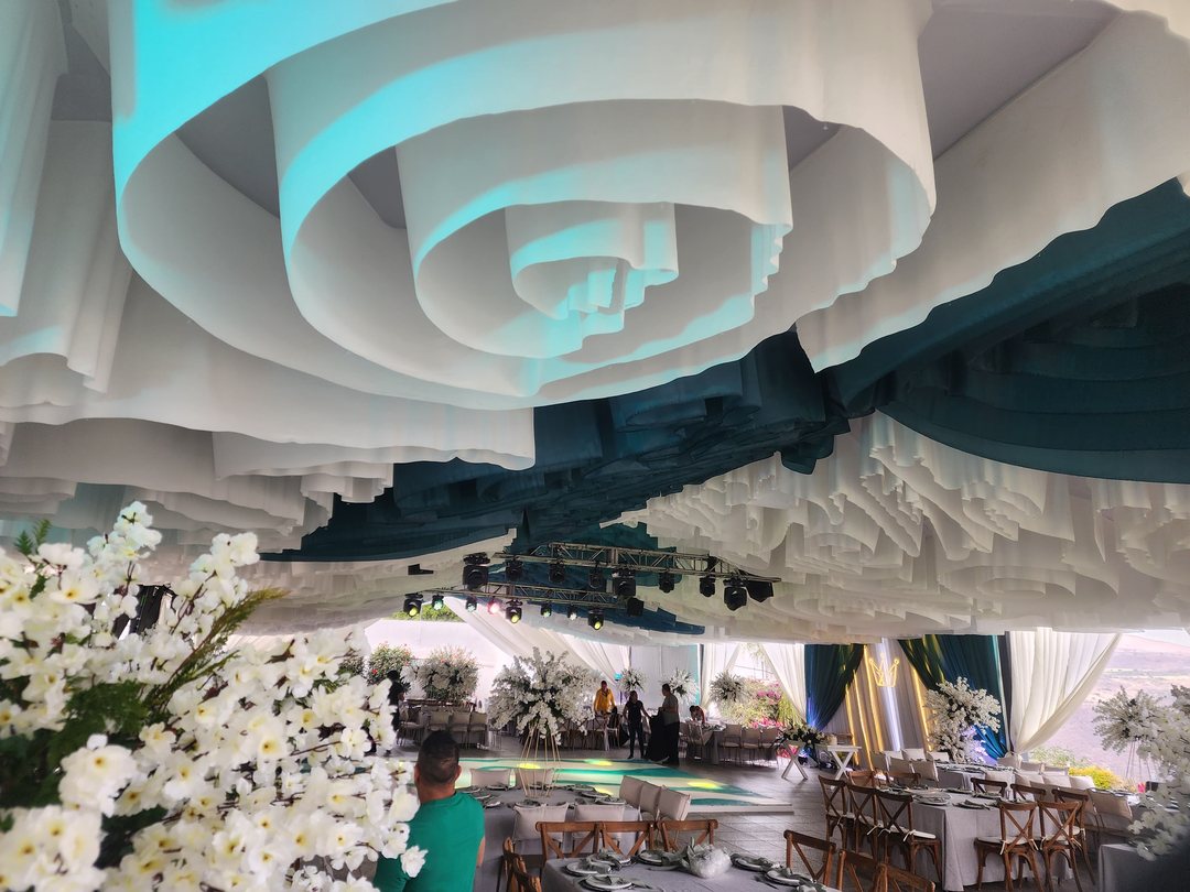 Techo de tela blanca en espiral con una franja turquesa sobre mesas con flor blanca