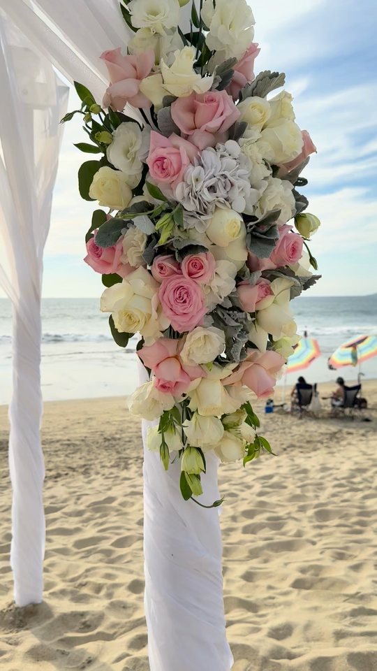 Acercamiento al ramo de flor rosa y blanca de un arco de ceremonia en la playa, con el mar al fondo