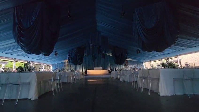 Carpa forrada de tela azul por fuera y por dentro, con techo drapeado azul sobre las mesas montadas