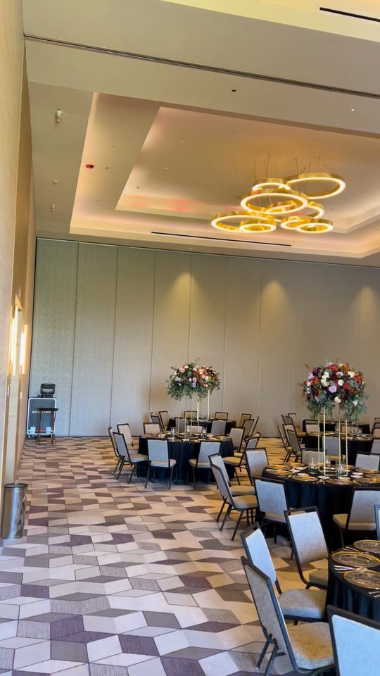 Salón con centros de mesa altos de flor otoñal sobre mesas negras y candiles de aros, Zapopan