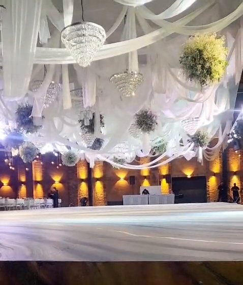 Techo drapeado de tela blanca con candiles de cristal y esferas de follaje sobre la pista, de noche