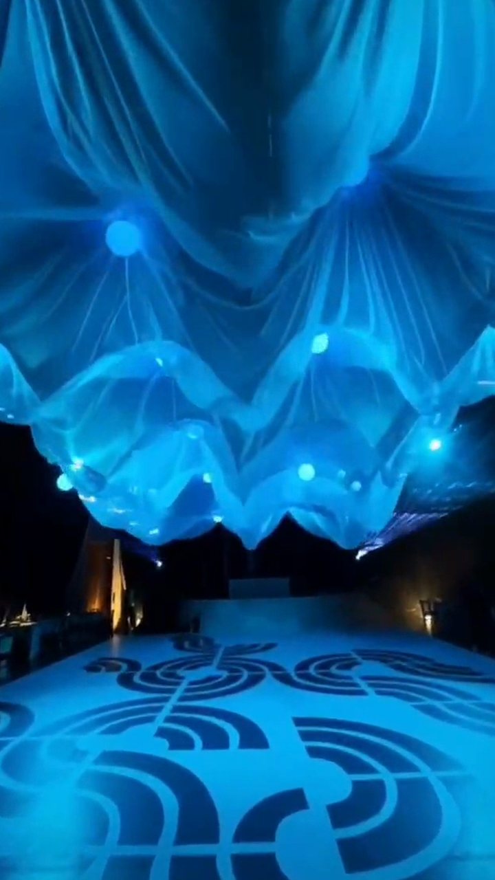 Entelado cinético azul: la tela sube y baja con esferas de luz sobre la pista, de noche
