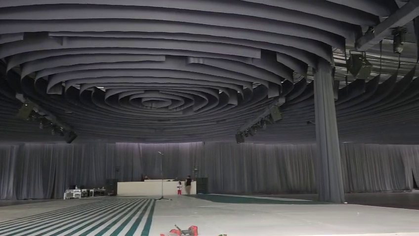 Techo de bandas de tela gris en espiral sobre un salón amplio con pista de rayas, durante el montaje